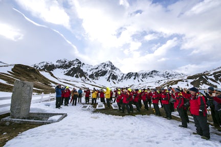 Toursits in red jackets stand in the snow around the grave of Sir Ernest Shackleton in Grytviken on South Georgia island